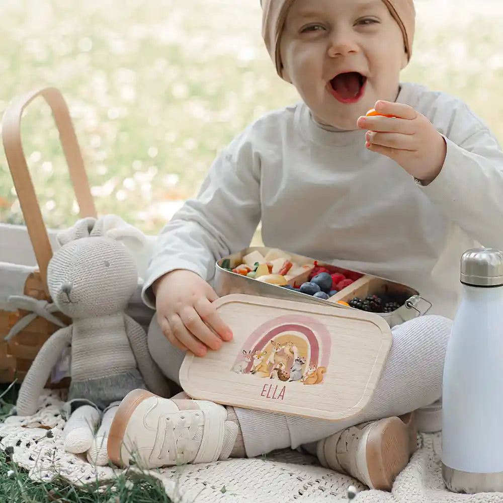 Junge sitzt auf Wiese mit Brotdose und lacht