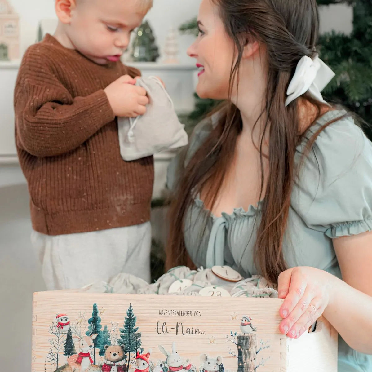 Gemütliche Adventsstimmung: Mutter hilft Kind beim Entdecken einer Überraschung im personalisierten Jutebeutel des Familienadventskalenders bei Kerzenschein